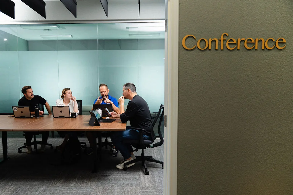 The signed Conference room at Corridor Collective, occupied, seen from the corridor through its glass wall