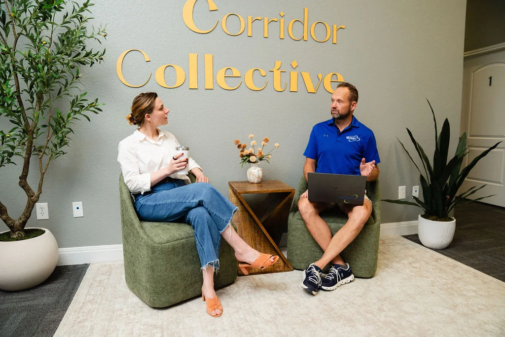The lobby lounge at Corridor Collective in San Marcos, with two people working on laptops beneath the Corridor Collective sign