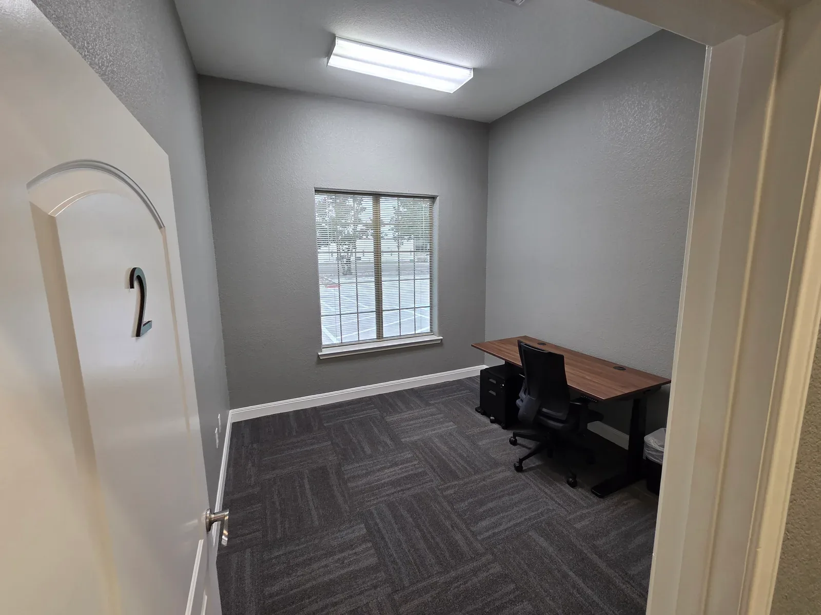 A furnished private office at Corridor Collective, 20 minutes from New Braunfels, with two desks and natural light from a window